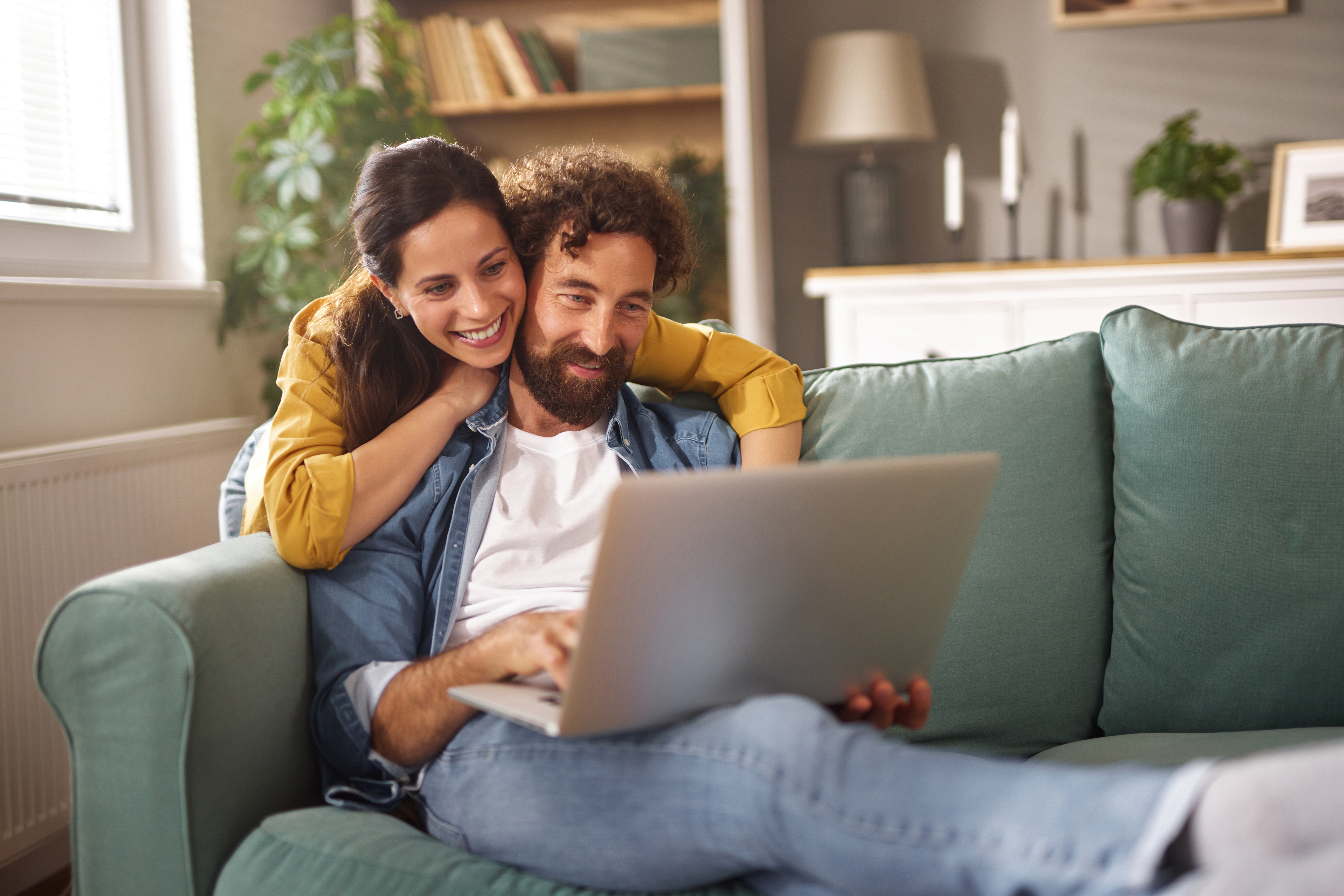 Smiling couple relaxing on sofa using laptop for a video call at home