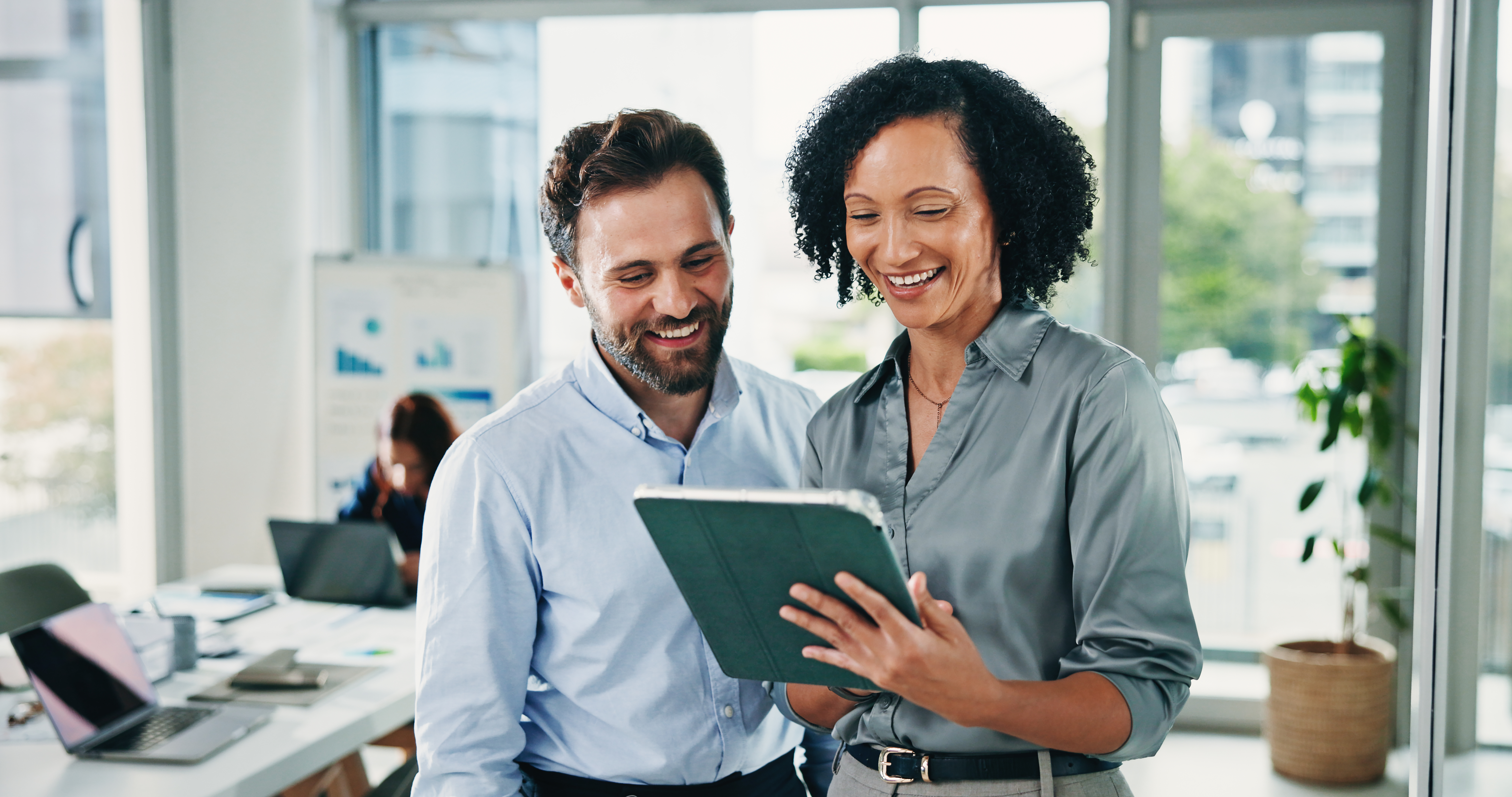 Happy woman, man and discussion with tablet at office for review, insight or notes at insurance company. People, broker and advisor on app, team and tech for project report at risk management agency